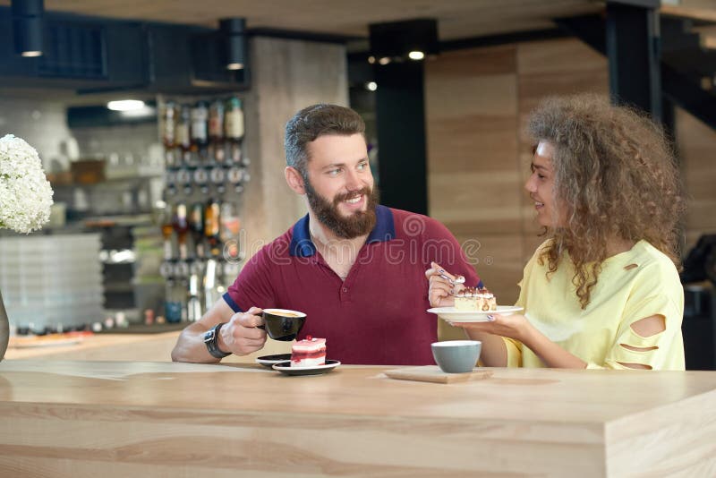 La coppia di risata di giovani studenti che bevono il caffè, mangiante agglutina in caffè fotografia stock La coppia di risata di giovani studenti che bevono il caffè, mangiante agglutina in caffè fotografia stock