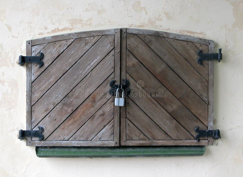 La couleur foncée naturelle a vieilli les volets lourds fermés par bois, verrouillés au grand cadenas de fer image libre de droits La couleur foncée naturelle a vieilli les volets lourds fermés par bois, verrouillés au grand cadenas de fer image libre de droits