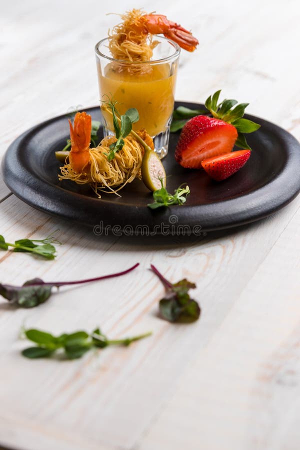 La crevette croustillante en croûte de Kataifi et le thym avec Champagne Sauce en verres et fraises se trouvent d'un plat noir su photo libre de droits La crevette croustillante en croûte de Kataifi et le thym avec Champagne Sauce en verres et fraises se trouvent d'un plat noir su photo libre de droits