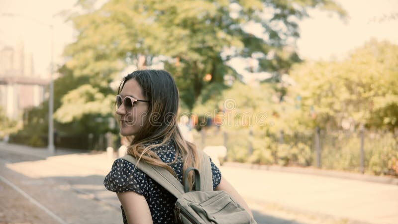 La cámara sigue la muchacha turística europea emocionada feliz con la mochila y la cámara en las gafas de sol sonrisa, dando vuel