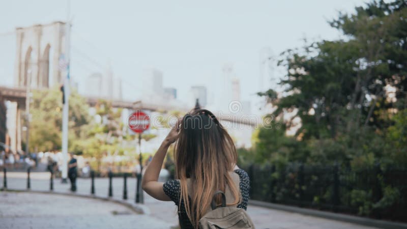 La cámara sigue a la muchacha turística europea emocionada juguetona con la mochila en las gafas de sol, aumentando las manos y 4