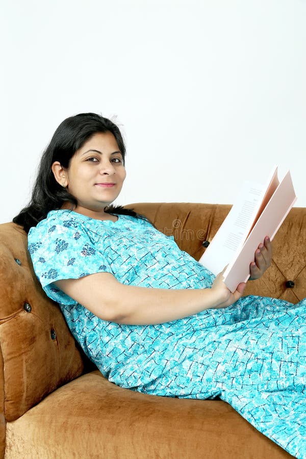 La dame enceinte tient le magazine de bébé à disposition avec se reposer sur le divan photo libre de droits La dame enceinte tient le magazine de bébé à disposition avec se reposer sur le divan photo libre de droits