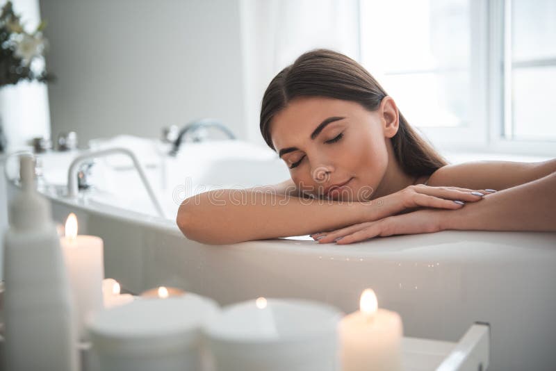 Portrait of serene female leaning on side of bath while resting there. Calm lady having leisure during spa procedure concept. Portrait of serene female leaning on side of bath while resting there. Calm lady having leisure during spa procedure concept