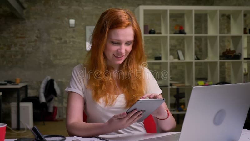 La dame mignonne de sourire de gingembre de caucasin est comprimé d'usinf, semblant créatif tout en se reposant dans le bureau lé banque de vidéos