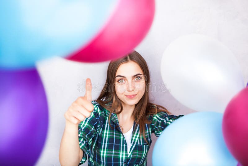 La demostración feliz de la mujer joven manosea con los dedos para arriba a través de los globos coloridos imagen de archivo La demostración feliz de la mujer joven manosea con los dedos para arriba a través de los globos coloridos imagen de archivo