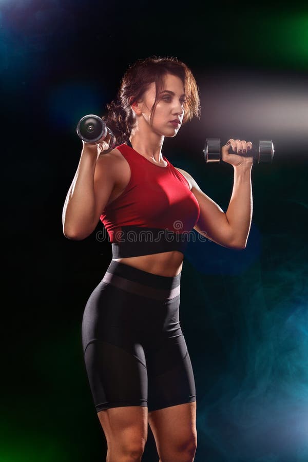 La donna adatta sportiva, atleta con le teste di legno fa gli esercizi di forma fisica su fondo nero immagini stock libere da diritti La donna adatta sportiva, atleta con le teste di legno fa gli esercizi di forma fisica su fondo nero immagini stock libere da diritti