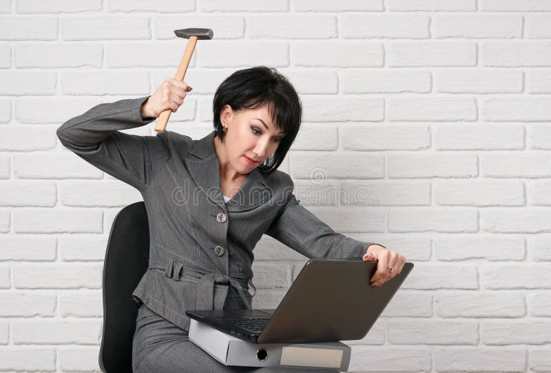 La donna arrabbiata di affari con il computer portatile e le cartelle che fanno vestirsi lo sforzo, in un vestito grigio posa dav fotografia stock libera da diritti La donna arrabbiata di affari con il computer portatile e le cartelle che fanno vestirsi lo sforzo, in un vestito grigio posa dav fotografia stock libera da diritti