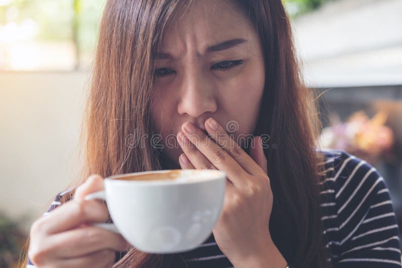 La donna asiatica si siede con il mento che riposa sulle suoi mani e closing lei occhi che odorano il caffè caldo sulla tavola di immagine stock La donna asiatica si siede con il mento che riposa sulle suoi mani e closing lei occhi che odorano il caffè caldo sulla tavola di immagine stock