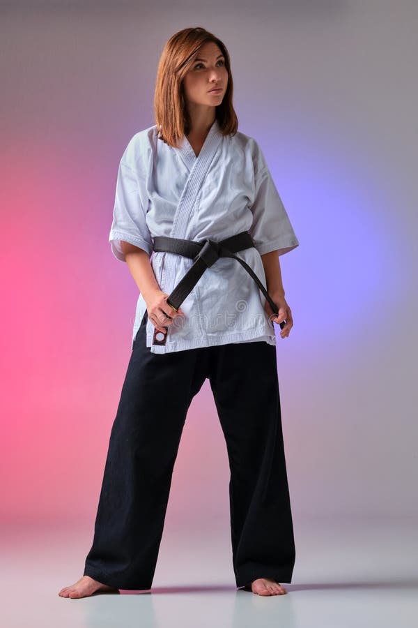 La donna atletica in kimono tradizionale sta praticando il karatè in studio fotografia stock La donna atletica in kimono tradizionale sta praticando il karatè in studio fotografia stock