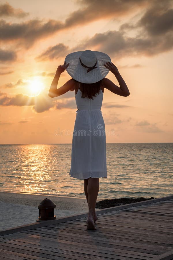 La donna attraente in vestito e cappello bianchi gode del tramonto immagine stock La donna attraente in vestito e cappello bianchi gode del tramonto immagine stock
