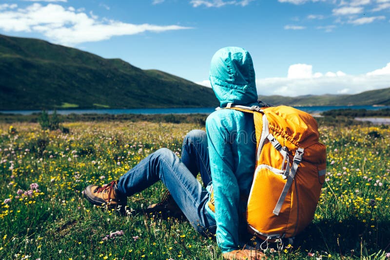 La donna Backpacking si siede sui fiori e sull'erba in montagne di elevata altitudine