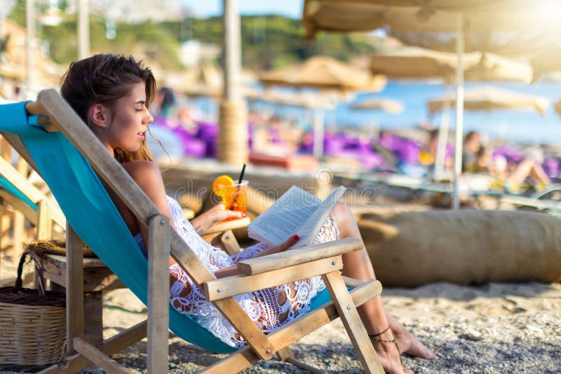 La donna bionda si rilassa in una sedia del sole su una spiaggia fotografia stock La donna bionda si rilassa in una sedia del sole su una spiaggia fotografia stock