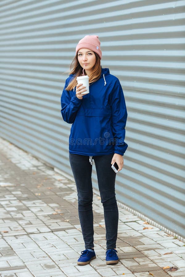La donna castana sportiva alla moda a urbano d'avanguardia outwear la posa con il giorno piovoso freddo dell'autunno della paglia