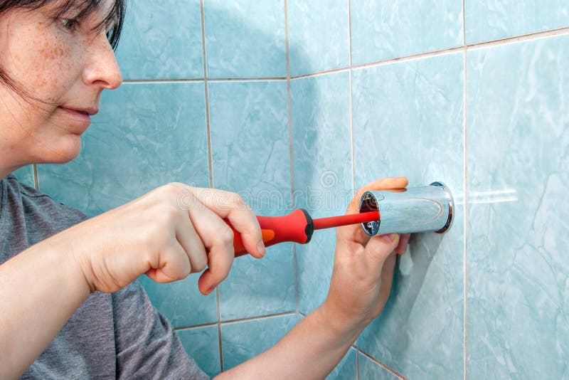 Replacing the plumbing in the bathroom, the woman fixed to the wall holder bracket for a shower, using a screwdriver. Replacing the plumbing in the bathroom, the woman fixed to the wall holder bracket for a shower, using a screwdriver.