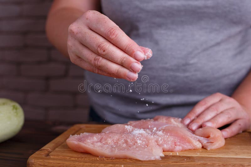 Overweight woman hands adding salt to raw chicken breasts. Dieting, healthy low calorie food, weight losing concept. Overweight woman hands adding salt to raw chicken breasts. Dieting, healthy low calorie food, weight losing concept