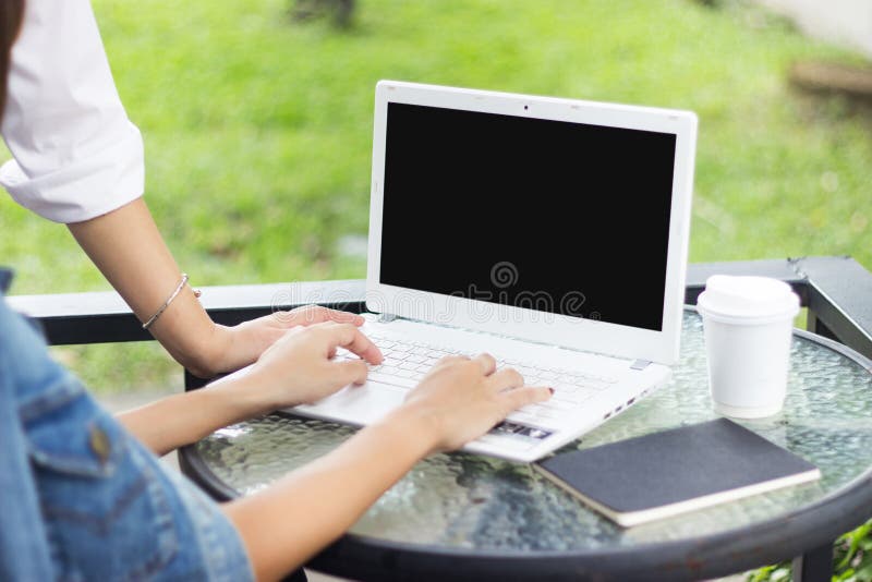 La donna due sta vedendo il computer portatile sulla tavola di vetro mentre scriveva sul cuscinetto con la tazza di carta nera de fotografia stock libera da diritti La donna due sta vedendo il computer portatile sulla tavola di vetro mentre scriveva sul cuscinetto con la tazza di carta nera de fotografia stock libera da diritti