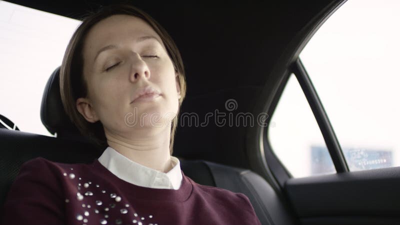 La donna graziosa con capelli marroni in blusa bianca e maglione marrone rossiccio ridinging nel traffico in automobile ed appena