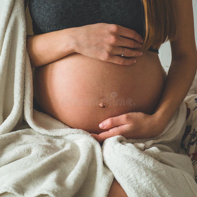 La donna incinta attraente sta sedendosi a letto e sta tenendo la sua pancia Ultimi mesi della gravidanza fotografia stock libera da diritti La donna incinta attraente sta sedendosi a letto e sta tenendo la sua pancia Ultimi mesi della gravidanza fotografia stock libera da diritti