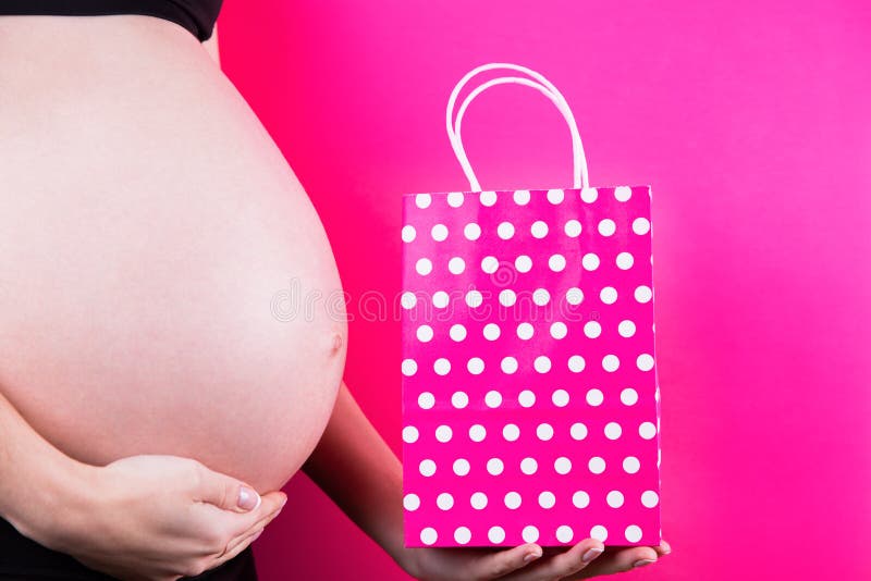 La donna incinta sta tenendo il sacchetto della spesa festivo in sua mano vicino alla pancia su fondo rosa fotografia stock libera da diritti La donna incinta sta tenendo il sacchetto della spesa festivo in sua mano vicino alla pancia su fondo rosa fotografia stock libera da diritti