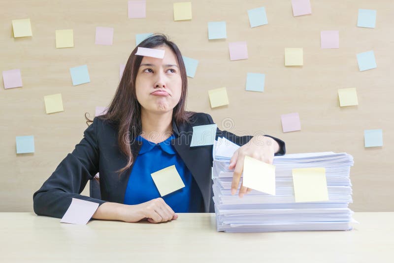 La donna lavoratrice del primo piano sta alesando dal mucchio della carta di lavoro e del duro lavoro davanti lei nel concetto de immagini stock La donna lavoratrice del primo piano sta alesando dal mucchio della carta di lavoro e del duro lavoro davanti lei nel concetto de immagini stock
