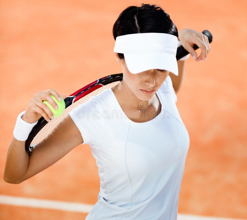 Woman in sports wear keeps tennis racket and ball on her shoulders at the clay tennis court. Leisure. Woman in sports wear keeps tennis racket and ball on her shoulders at the clay tennis court. Leisure