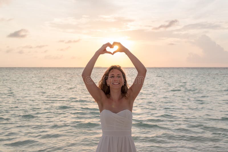 La donna nei telai di luna di miele passa in forma del cuore, struttura del cuore del dito guardando e sorridere alla macchina fo fotografia stock libera da diritti La donna nei telai di luna di miele passa in forma del cuore, struttura del cuore del dito guardando e sorridere alla macchina fo fotografia stock libera da diritti