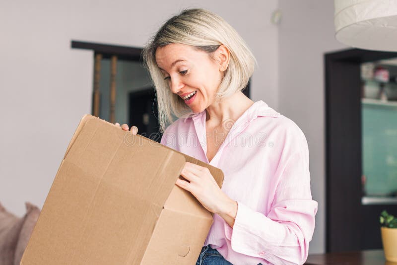 La donna seduta sul divano a casa, aprendo il cartone, ha ricevuto un pacco pacco immagini stock