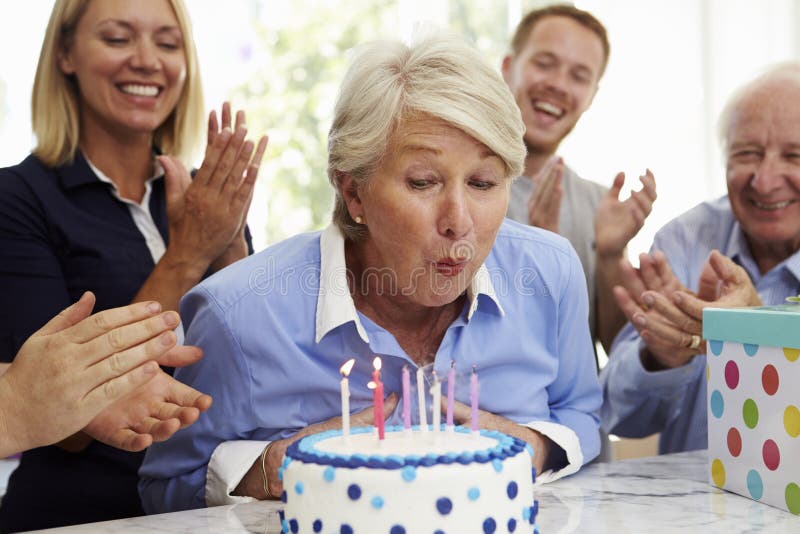 La donna senior spegne le candele della torta di compleanno alla festa di famiglia fotografia stock libera da diritti La donna senior spegne le candele della torta di compleanno alla festa di famiglia fotografia stock libera da diritti