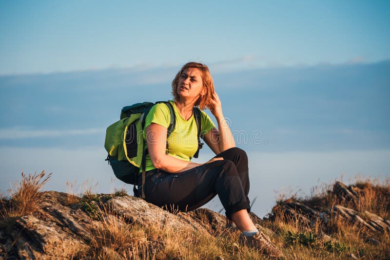 La donna si siede sulla scogliera ed esamina le cime fotografia stock La donna si siede sulla scogliera ed esamina le cime fotografia stock