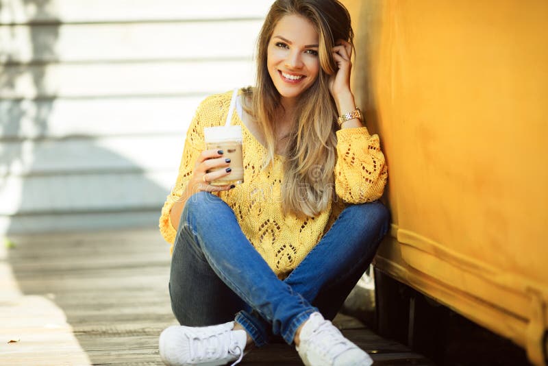 La donna sorridente felice sta indossando il caffè bevente del maglione giallo vicino al vecchio retro bus fotografia stock La donna sorridente felice sta indossando il caffè bevente del maglione giallo vicino al vecchio retro bus fotografia stock