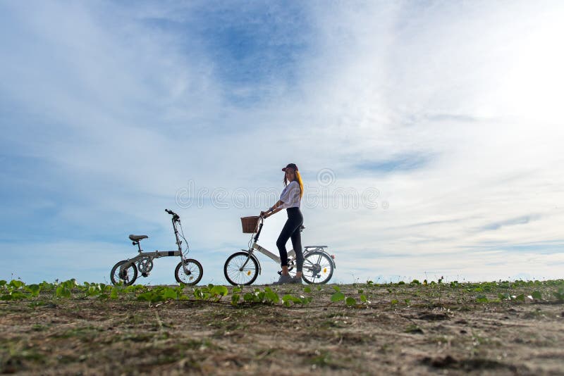 La donna sorridente gode di e si rilassa con la guida della bicicletta sulla sabbia della spiaggia divertendosi e felice, fondo d fotografia stock libera da diritti La donna sorridente gode di e si rilassa con la guida della bicicletta sulla sabbia della spiaggia divertendosi e felice, fondo d fotografia stock libera da diritti