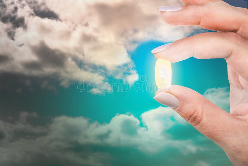 La donna sta tenendo le sue dita una capsula antidepressiva contro il cielo blu Uscita dalla depressione immagine stock libera da diritti La donna sta tenendo le sue dita una capsula antidepressiva contro il cielo blu Uscita dalla depressione immagine stock libera da diritti