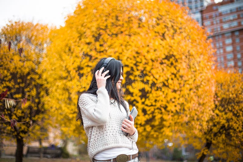 La donna teenager felice che ascolta la musica e si rilassa nel parco di autunno Alberi gialli, bello tempo di caduta immagini stock libere da diritti La donna teenager felice che ascolta la musica e si rilassa nel parco di autunno Alberi gialli, bello tempo di caduta immagini stock libere da diritti