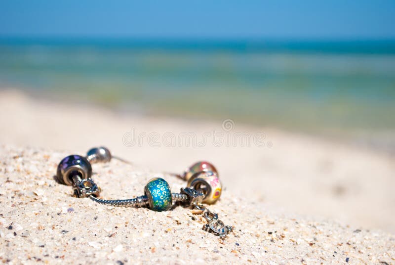 La décoration femelle de bracelet se trouve sur le sable sur un fond de mer bleue et de ciel bleu image libre de droits La décoration femelle de bracelet se trouve sur le sable sur un fond de mer bleue et de ciel bleu image libre de droits