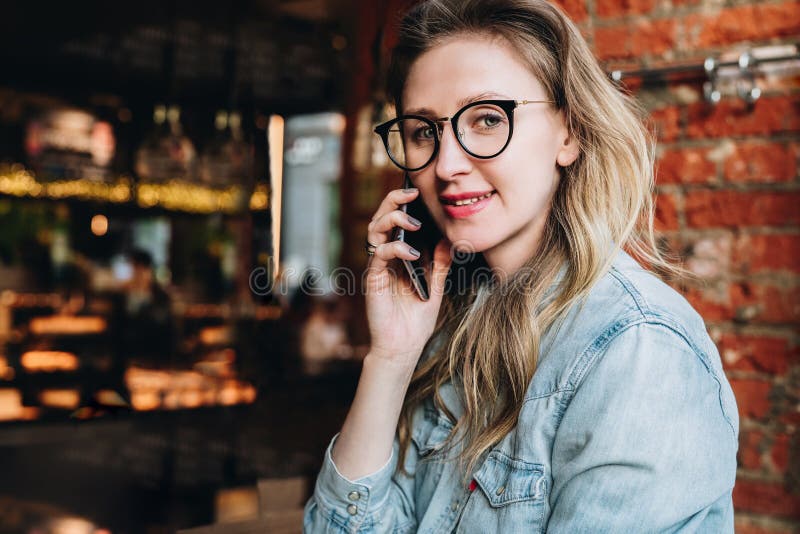 La empresaria joven tiene conversaciones telefónicas Blogger alegre de la muchacha en los vidrios de moda que se sientan en el ca imagen de archivo La empresaria joven tiene conversaciones telefónicas Blogger alegre de la muchacha en los vidrios de moda que se sientan en el ca imagen de archivo