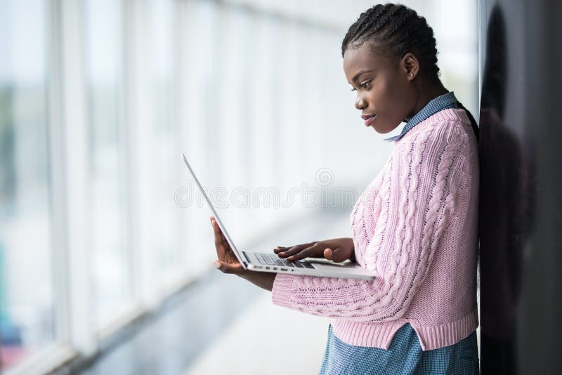 La estudiante afroamericana de la belleza joven en los vidrios que sostienen el ordenador portátil y que estudian se prepara para imagen de archivo libre de regalías La estudiante afroamericana de la belleza joven en los vidrios que sostienen el ordenador portátil y que estudian se prepara para imagen de archivo libre de regalías