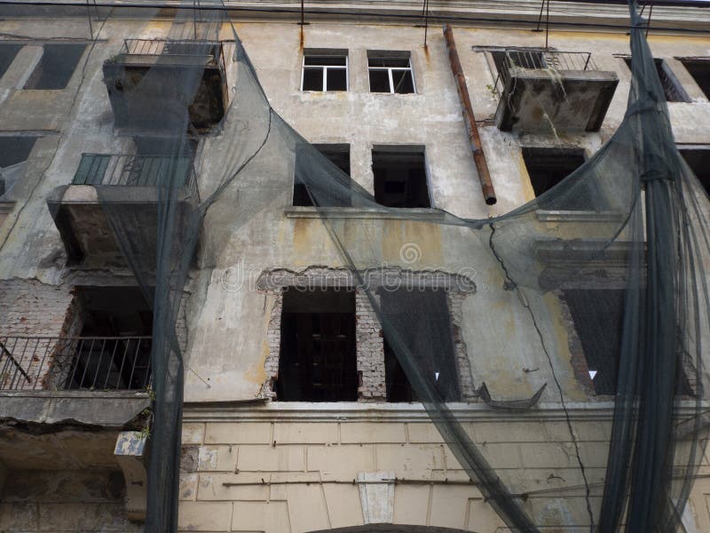 La facciata di un edificio abbandonato in rovina con vetri rotti e stoffa appesa ai muri, l'orrore del film immagine stock La facciata di un edificio abbandonato in rovina con vetri rotti e stoffa appesa ai muri, l'orrore del film immagine stock