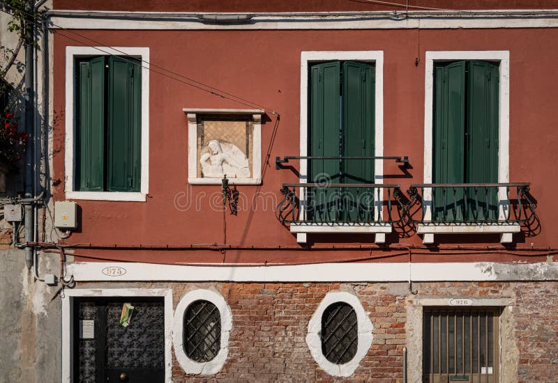 La facciata rossa veneziana di una vecchia casa con scene religiose, finestre verdi e tipiche finestre ovaiole Venezia, Italia fotografia stock libera da diritti La facciata rossa veneziana di una vecchia casa con scene religiose, finestre verdi e tipiche finestre ovaiole Venezia, Italia fotografia stock libera da diritti