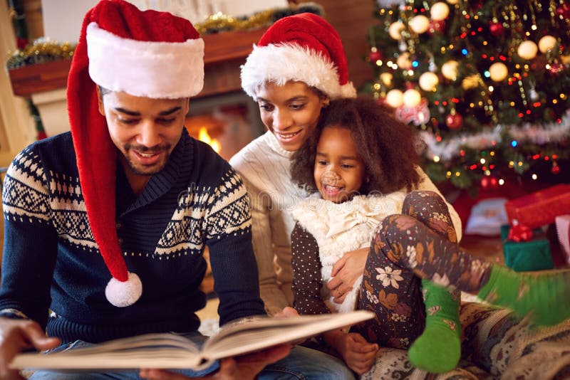 La famiglia afroamericana felice ha letto un libro al camino sul Natale immagine stock La famiglia afroamericana felice ha letto un libro al camino sul Natale immagine stock
