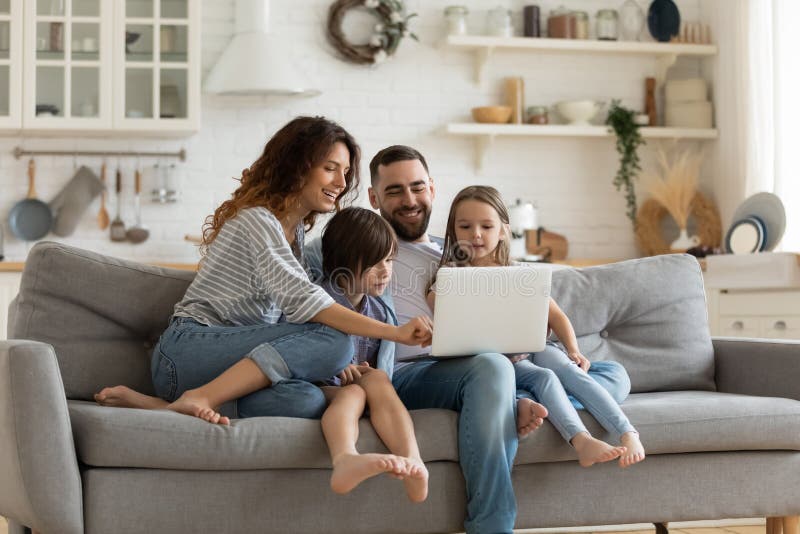 La famiglia felice con i bambini si siede sul divano utilizzando il computer portatile