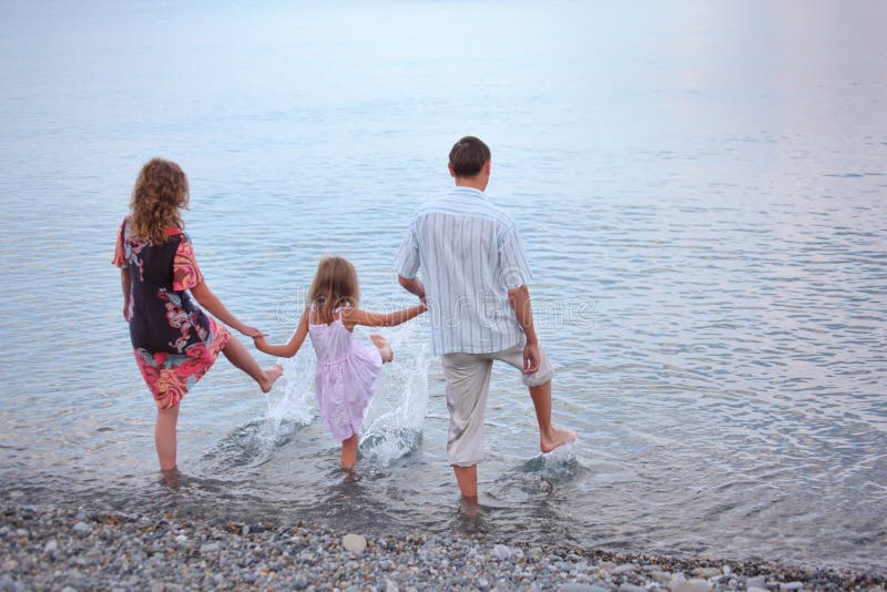 La famiglia felice con la ragazza sulla spiaggia va in acqua fotografia stock libera da diritti La famiglia felice con la ragazza sulla spiaggia va in acqua fotografia stock libera da diritti