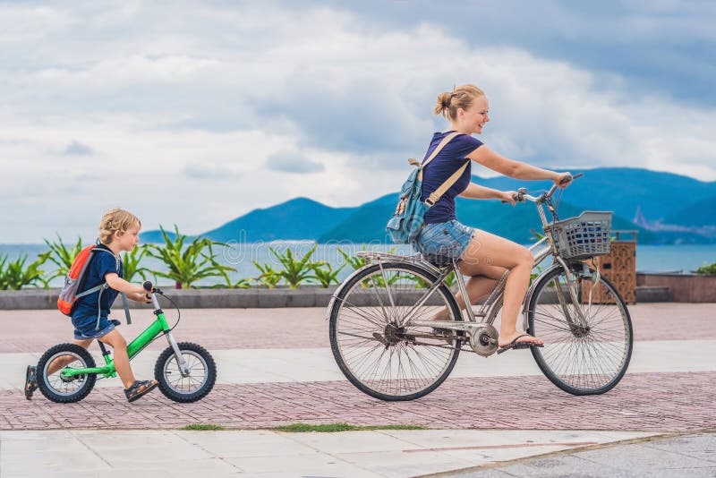La famiglia felice sta guidando le bici all'aperto e sorridere Mamma su una bici fotografie stock libere da diritti La famiglia felice sta guidando le bici all'aperto e sorridere Mamma su una bici fotografie stock libere da diritti