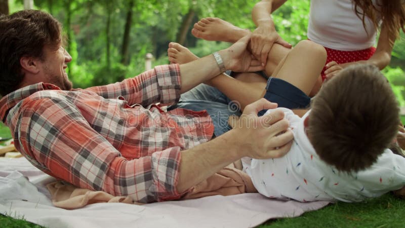 La famiglia gioca insieme nel parco estivo. genitori che solleticano i bambini all'aperto