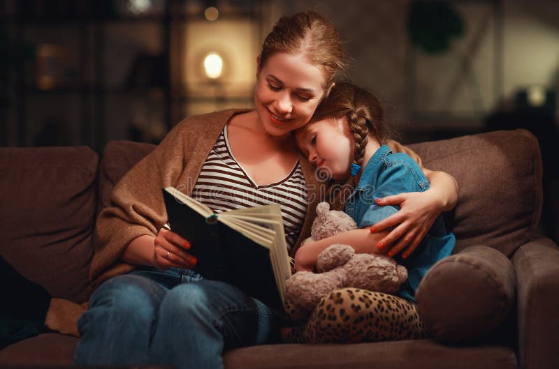 La familia antes de la madre que se va a la cama lee a su libro de la hija del ni?o cerca de una l?mpara por la tarde imágenes de archivo libres de regalías La familia antes de la madre que se va a la cama lee a su libro de la hija del ni?o cerca de una l?mpara por la tarde imágenes de archivo libres de regalías
