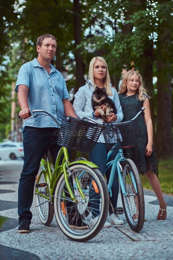 La familia atractiva se vistió en ropa casual en un paseo de la bicicleta con su pequeño perro lindo del perro de Pomerania imágenes de archivo libres de regalías La familia atractiva se vistió en ropa casual en un paseo de la bicicleta con su pequeño perro lindo del perro de Pomerania imágenes de archivo libres de regalías