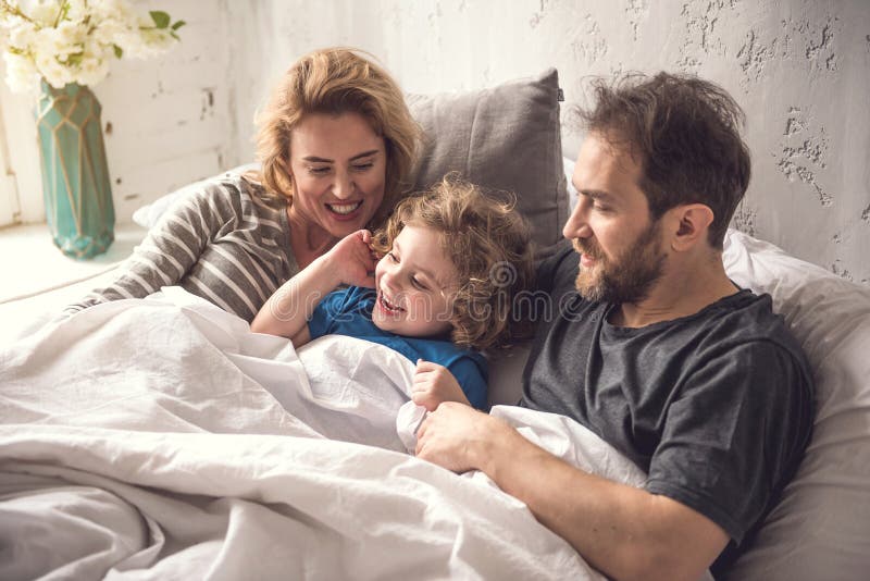 La familia bendecida está comenzando nuevo día en común en dormitorio brillante fotografía de archivo libre de regalías La familia bendecida está comenzando nuevo día en común en dormitorio brillante fotografía de archivo libre de regalías