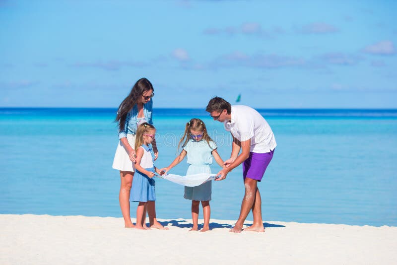La familia feliz con el mapa encuentra la manera en la playa foto de archivo La familia feliz con el mapa encuentra la manera en la playa foto de archivo
