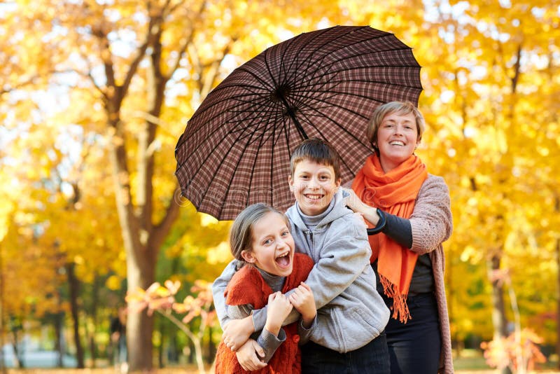 La familia feliz está en parque de la ciudad del otoño La gente está presentando debajo del paraguas Los niños y los padres están fotografía de archivo libre de regalías La familia feliz está en parque de la ciudad del otoño La gente está presentando debajo del paraguas Los niños y los padres están fotografía de archivo libre de regalías