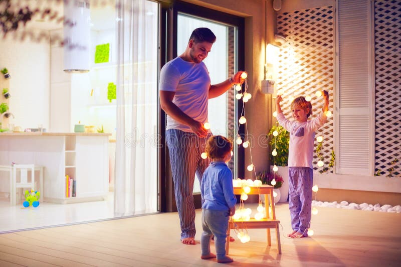 La familia feliz, padre con los hijos adorna área del patio del espacio abierto con las guirnaldas de la Navidad fotografía de archivo La familia feliz, padre con los hijos adorna área del patio del espacio abierto con las guirnaldas de la Navidad fotografía de archivo