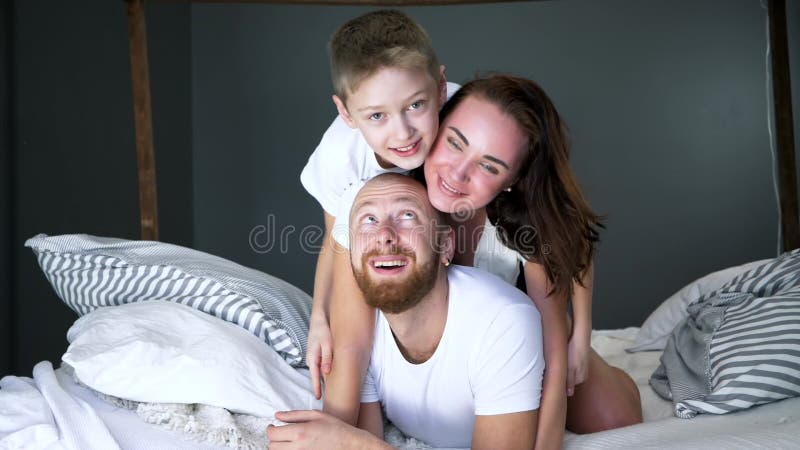 La famille heureuse dans le T-shirts blanc se trouvent sur l'un l'autre sur le lit à la maison dans la chambre